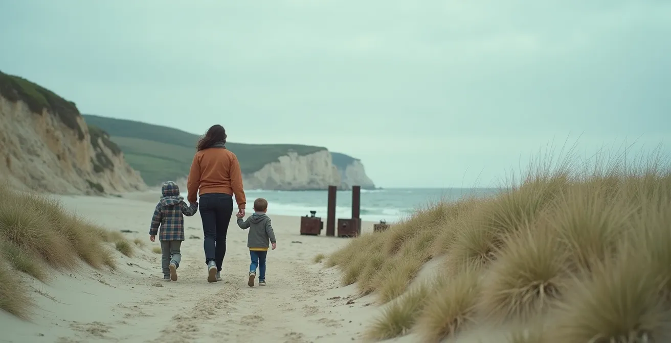 Parents et enfants marchant sur une plage de Normandie avec vestiges du Débarquement en arrière-plan